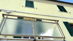 Um edifício com fachada amarela, persianas verdes e uma grande janela com moldura de metal.