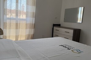 A bedroom with a bed, a nightstand, a dresser, and a mirror on the wall.