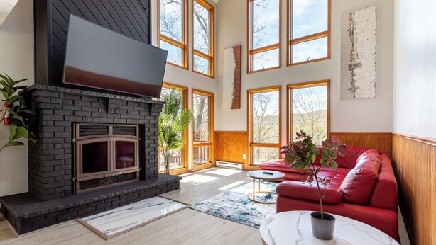 A spacious living room with a fireplace, large windows, a red sofa, and a marble coffee table. - Beautiful Modern Lodge! Pool Table,8 TVs Wi-Fi, Linen provided, Central AC (Saw Creek)