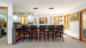 A modern kitchen with a central island, bar stools, and a dining area with a view of the outdoors. - Beautiful Modern Lodge! Pool Table,8 TVs Wi-Fi, Linen provided, Central AC (Saw Creek)