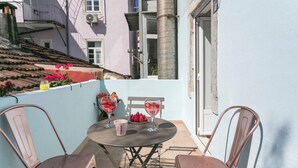 A small outdoor patio with a round table and two chairs, a bowl of strawberries, and two glasses of pink drink.