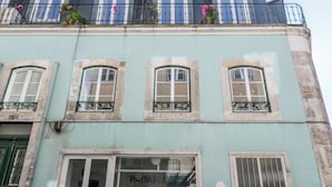 A building with a ground-floor shop, multiple windows, and a balcony with plants.