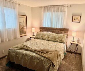 Une chambre à coucher bien aménagée, avec un grand lit, deux tables de chevet dotées de lampes et des œuvres d’art encadrées accrochées aux murs.