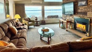 Een gezellige woonkamer met een leren bank, een glazen salontafel, een open haard en uitzicht op zee.