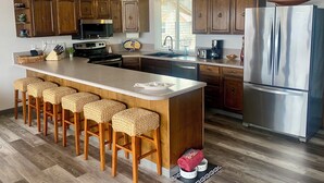 Een moderne keuken met houten kastjes, een roestvrijstalen koelkast, een groot eiland met barstoelen en hangende吊り下げ灯