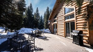 Una cabaña de troncos con terraza, asientos exteriores y una parrilla.