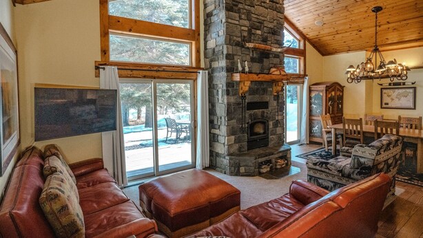 Una sala de estar acogedora con chimenea de piedra, sofás de cuero y grandes ventanales con vistas al exterior.