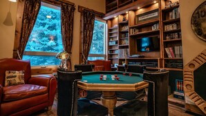 Una habitación acogedora con mesa de billar, sillones de cuero y una estantería llena de libros y DVD.