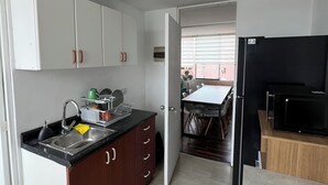 Een moderne keuken met witte kasten, een zwart aanrecht en een RVS spoelbak. Een eethoek met een tafel en stoelen is zichtbaar door een open deur.