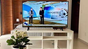 A modern living room with a television displaying a sports program, a white entertainment unit, and a potted plant on a wooden table. - Beautiful loft in amazing Guadalajara with AC, WiFi, fitness room, and workspace (Guadalajara)