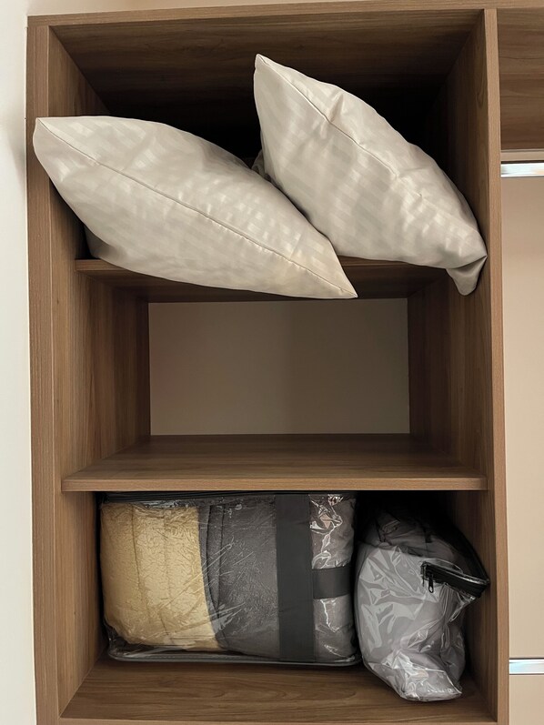 Un meuble de rangement en bois, avec deux coussins et une couverture enroulée.
