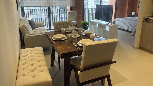 A modern living room with a dining area, a sofa, a TV, and a balcony with a view of buildings. - Beautiful loft in amazing Guadalajara with AC, WiFi, fitness room, and workspace (Guadalajara)