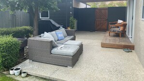 En täckt uteplats med en soffa i rotting, en träbänk och en grill.