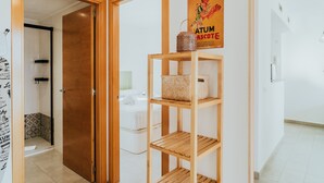 A hotel room with a wooden door, a shelf with baskets, a poster on the wall, and a white bed. - WELCS APARTAMENTO 206 EMP cerca del mar (Rosas / Roses)