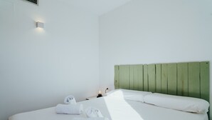 A neatly made bed with white linens and towels, a green headboard, and a wall-mounted light fixture. - WELCS APARTAMENTO 206 EMP cerca del mar (Rosas / Roses)