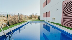 A swimming pool with a clear blue water surface, surrounded by a green lawn and a fence. - WELCS APARTAMENTO 206 EMP cerca del mar (Rosas / Roses)