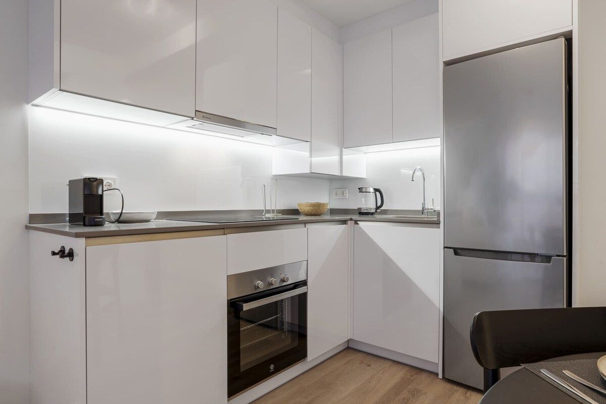 A modern kitchen with white cabinets, a stainless steel refrigerator, a built-in oven, and a coffee maker on the countertop.