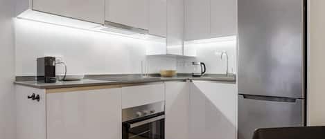 A modern kitchen with white cabinets, a stainless steel refrigerator, a built-in oven, and a coffee maker on the countertop.
