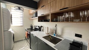 A compact kitchen with a built-in oven, microwave, and sink. There are wooden cabinets and a countertop with a dish rack.