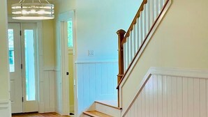 Un couloir doté d’un plancher en bois, d’un escalier avec des rampes blanches et d’un luminaire au plafond.