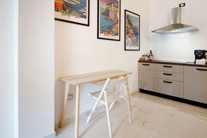 A kitchen with a wooden table, a white chair, a stainless steel range hood, and framed artwork on the wall. - Apartment 'Sempresole In Piazzetta' with Mountain View, Wi-Fi and Air Conditioning (Salerno)