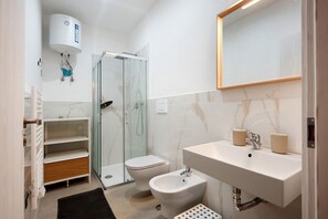 A modern bathroom with a glass shower enclosure, a toilet, a bidet, a sink with two cups, and a white toilet paper holder. - Apartment 'Sempresole In Piazzetta' with Mountain View, Wi-Fi and Air Conditioning (Salerno)