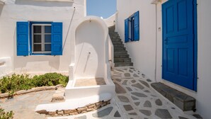A white building with blue doors and shutters, a stone staircase, and a small garden area. - Apartment 'Blue Dolphin Family Pool' with Sea View, Wi-Fi and Air Conditioning (Ag. Georgios)