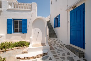 A white building with blue doors and shutters, a stone staircase, and a small garden area.