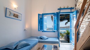 A room with a bed, a small table, and a view of the sea through an open door. - Apartment 'Blue Dolphin Family Pool' with Sea View, Wi-Fi and Air Conditioning (Ag. Georgios)