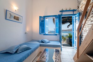 A room with a bed, a small table, and a view of the sea through an open door.