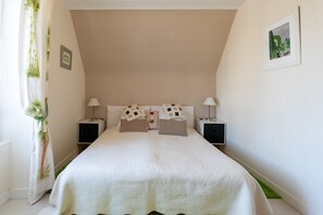 A bedroom with a bed, two bedside tables, a nightstand, a wall-mounted picture, and a curtain with a plant design.