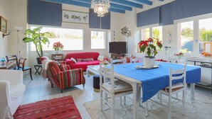 A dining area with a table set for two, a red sofa, striped armchairs, and a chandelier.
