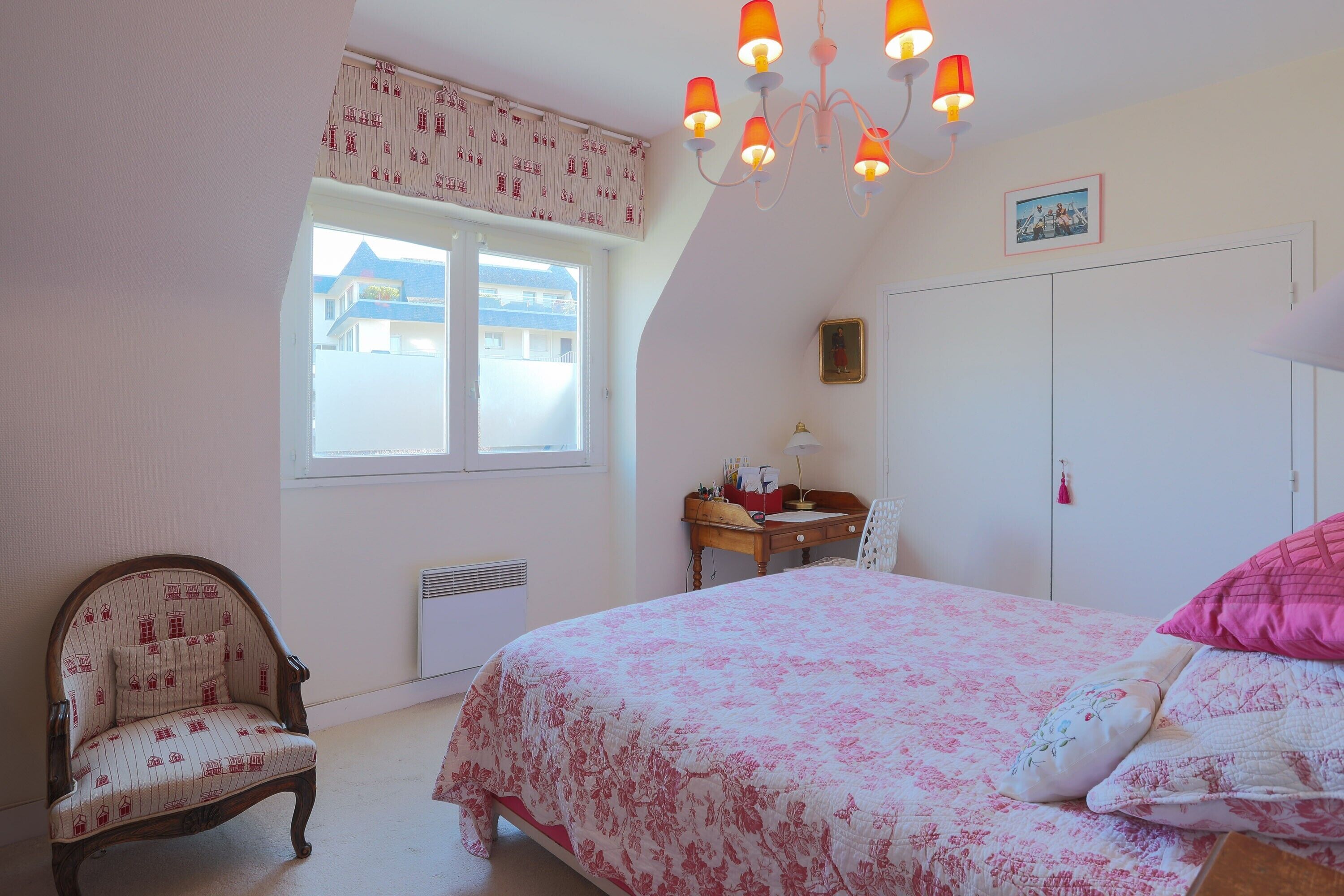 A bedroom with a bed, a chair, a desk, a window, and a door.