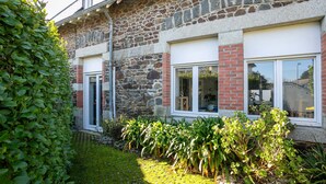 A stone building with a brick lower section, large windows, and a well-maintained garden with various plants.