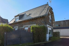 A stone house with a gated driveway, a small window, and a chimney.