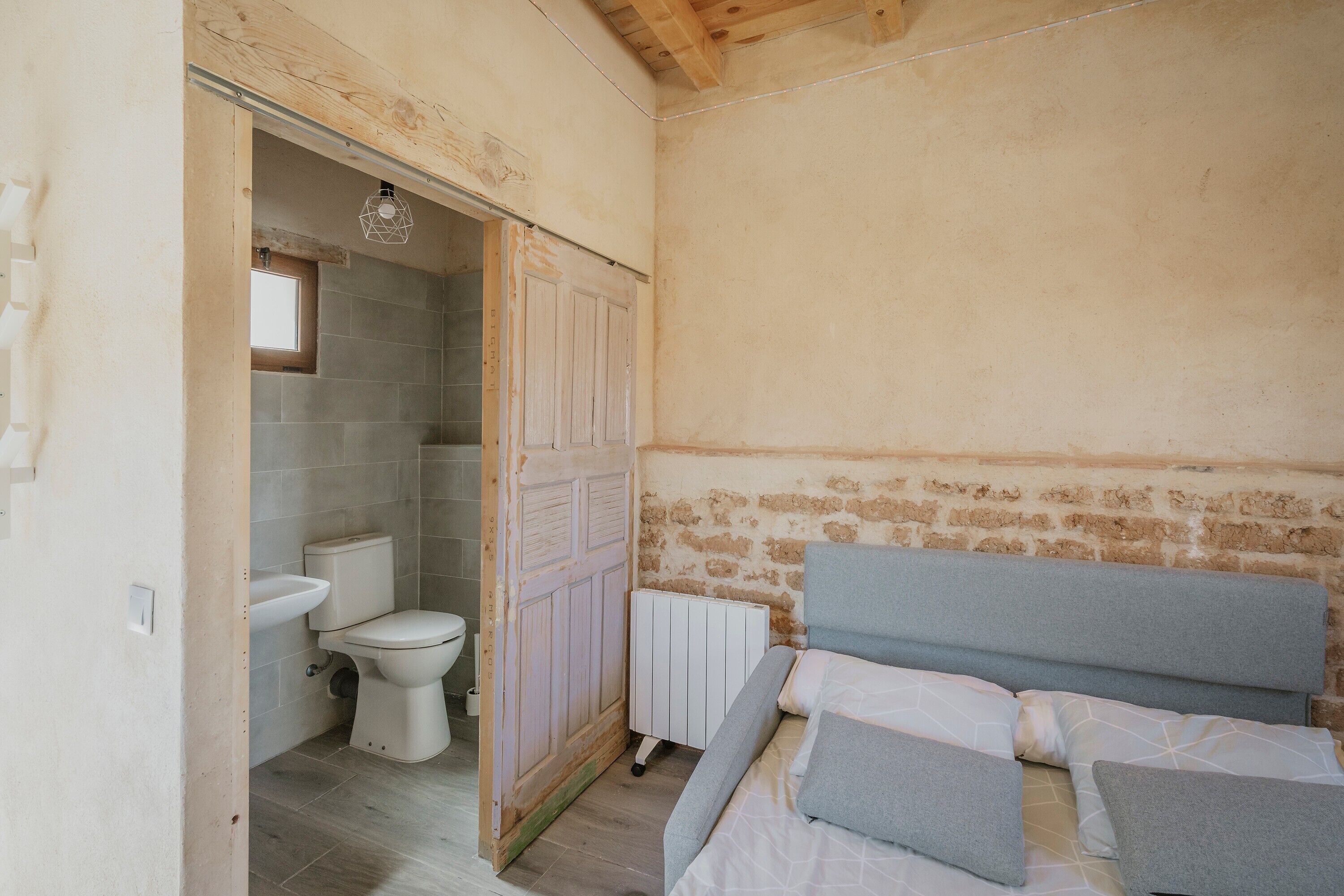 A bedroom with a bed, a window, a door, and a bathroom with a toilet and sink.