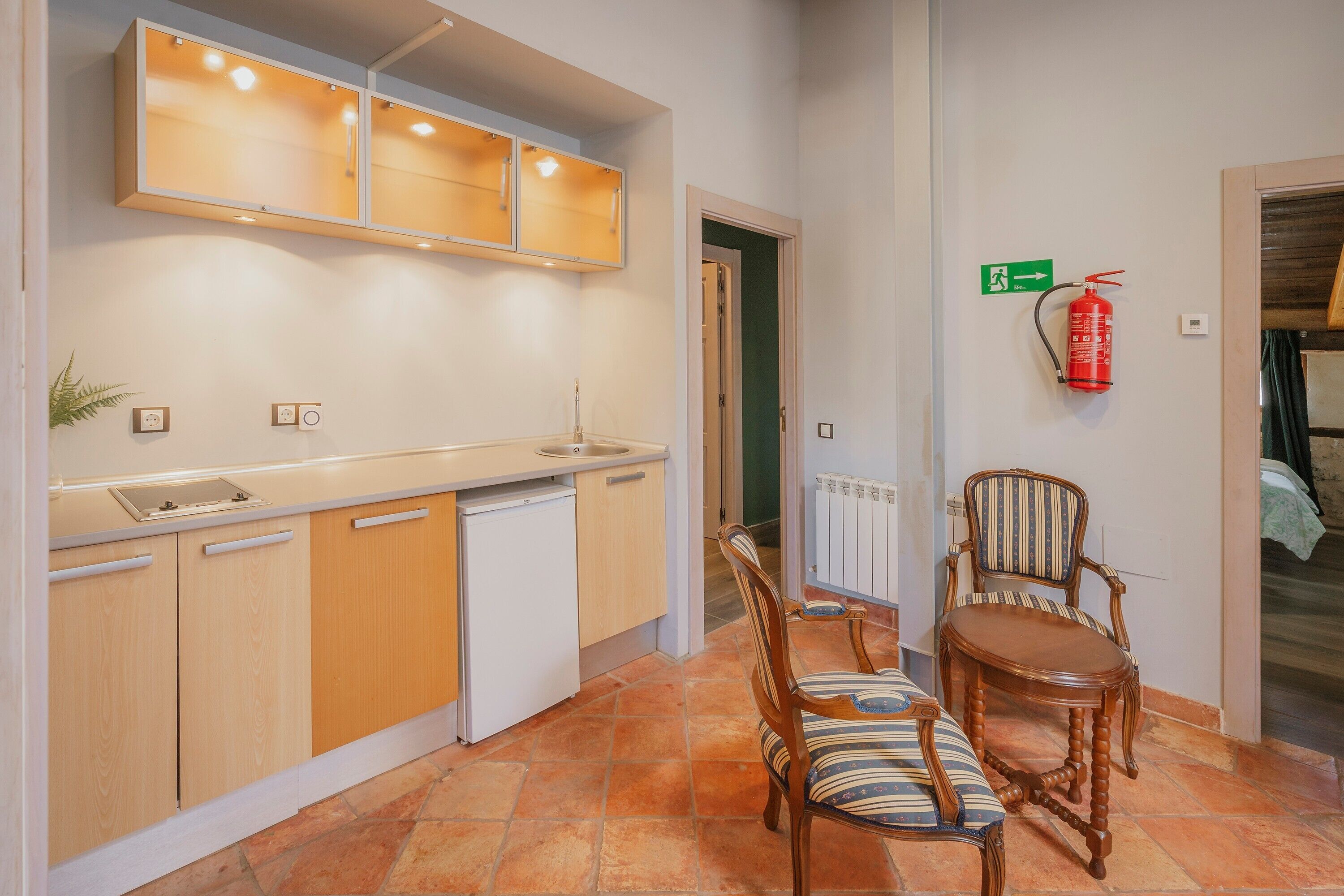 Una cocina compacta con armarios de madera, una encimera blanca, un lavamanos pequeño y una zona de comedor con sillas a rayas.