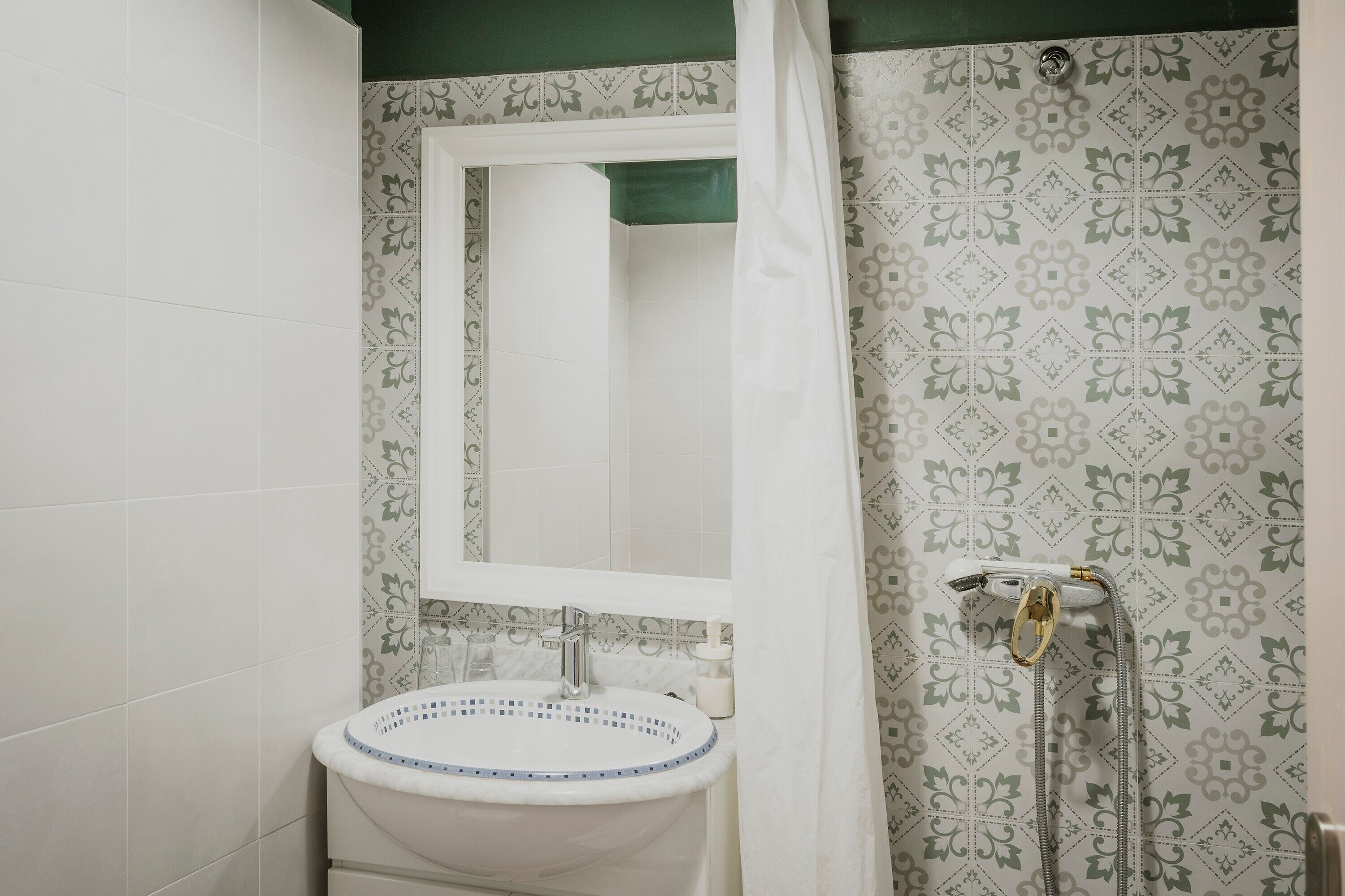 Un bagno con lavandino, specchio, doccia e piastrelle decorate.
