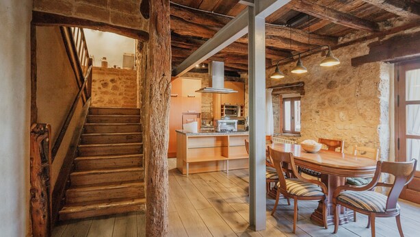 A rustic interior with a wooden staircase, a kitchen area with modern appliances, and a dining table with chairs.