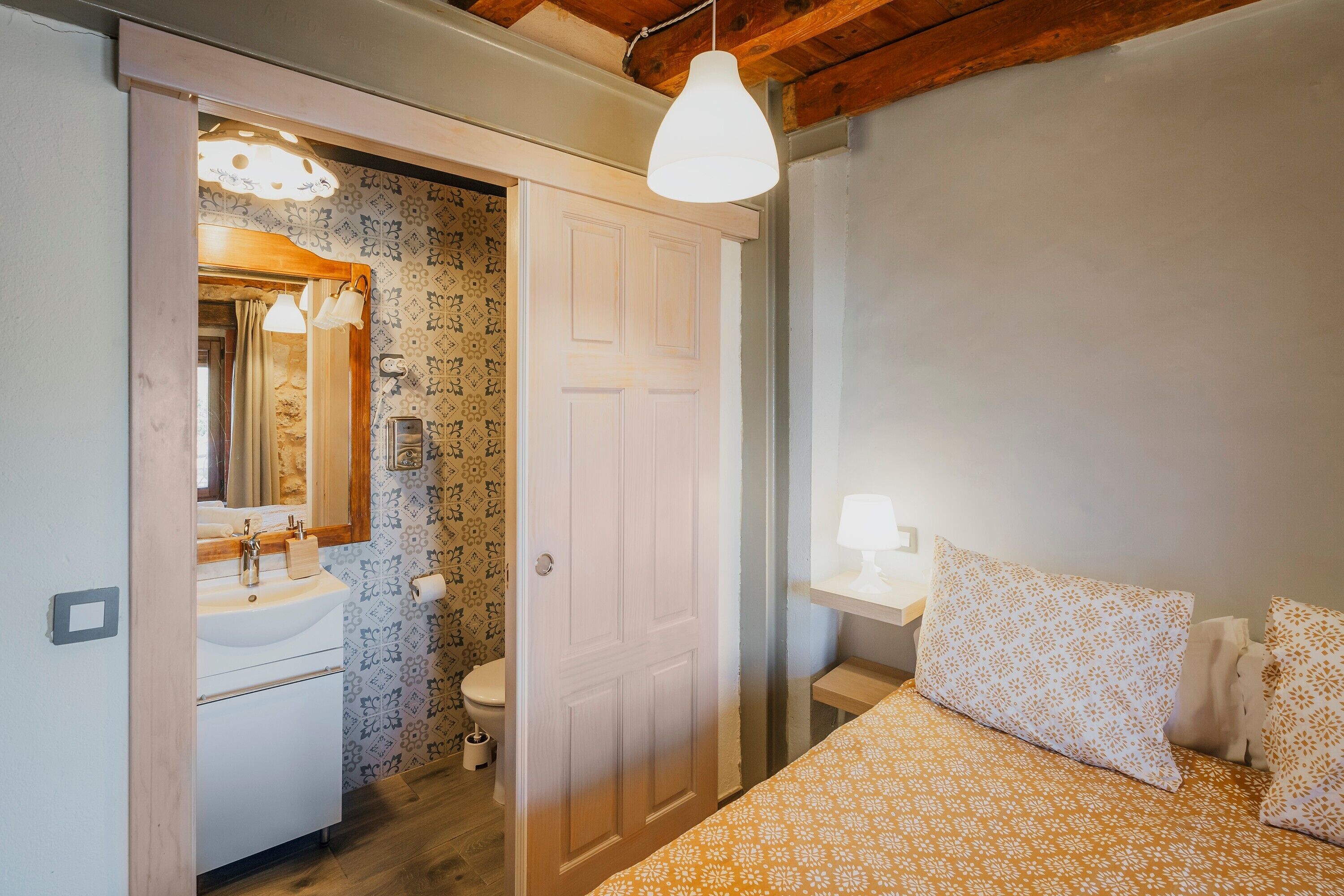 Un dormitorio con cama, mesita de noche y baño con lavamanos e inodoro.