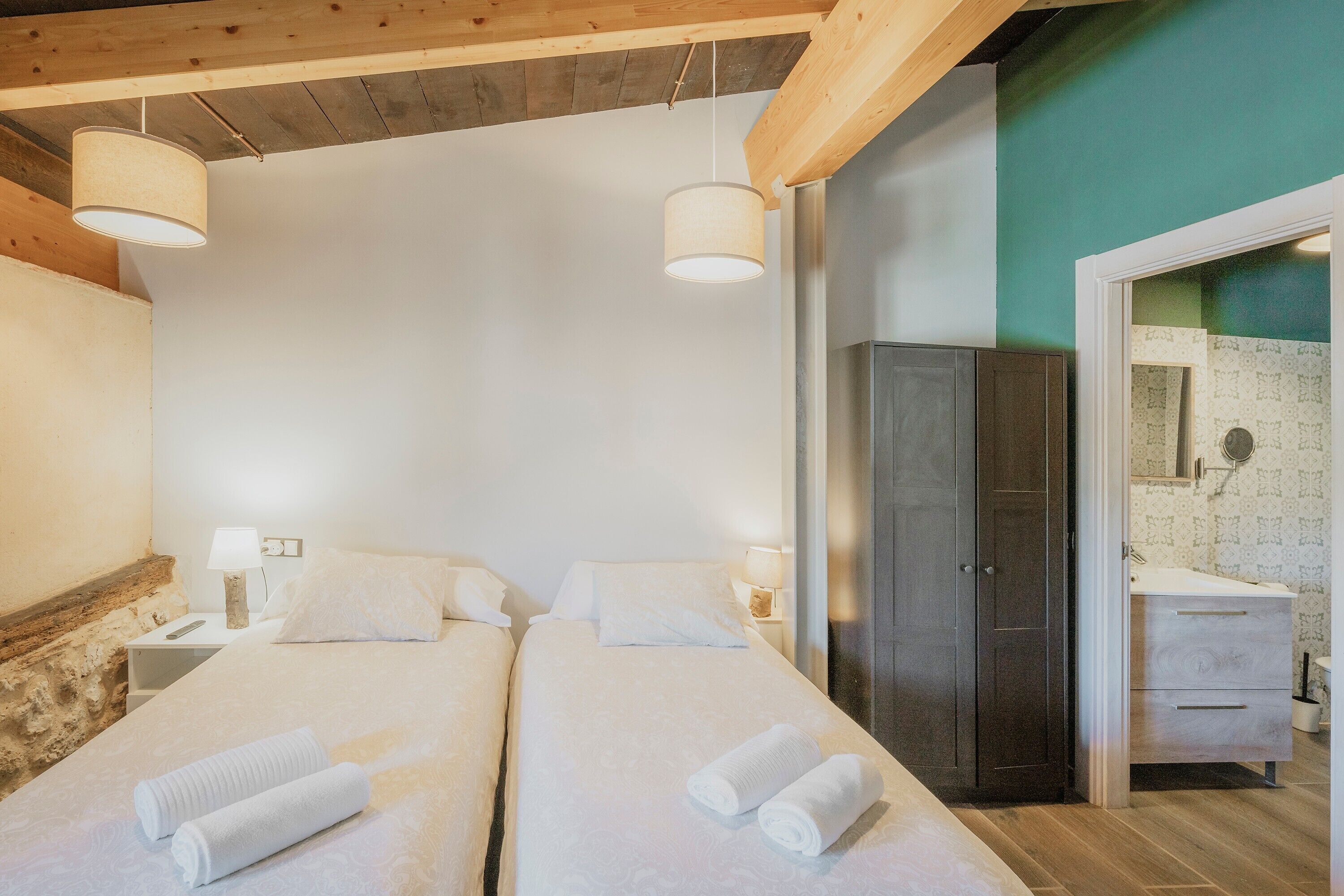 A room with two beds, a wardrobe, a bathroom with patterned tiles, and wooden beams on the ceiling.
