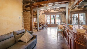 A rustic interior with exposed wooden beams, a stone wall, a wooden dining table with chairs, and a bar area with a mirror.