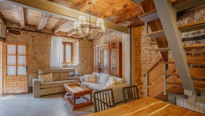 A rustic interior with a wooden dining table, two sofas, a chandelier, and a staircase.