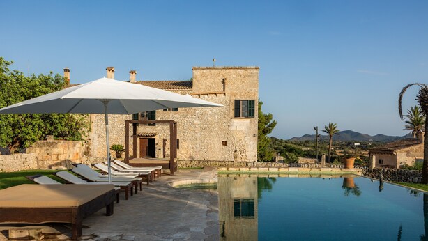 A stone building with a pool, lounge chairs, and umbrellas.