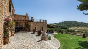 A stone building with a patio, outdoor seating, and a view of a hilly landscape.
