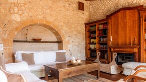 A stone-walled room with a fireplace, a wooden bookshelf, and a white sofa.