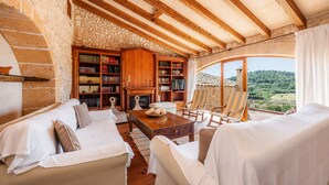 A cozy living room with a fireplace, bookshelves, and a view of the countryside.