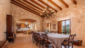 A spacious dining area with a large table, wooden chairs, stone walls, and a chandelier.