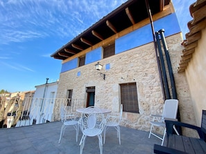 A stone building with a balcony, outdoor seating, and a clear blue sky.