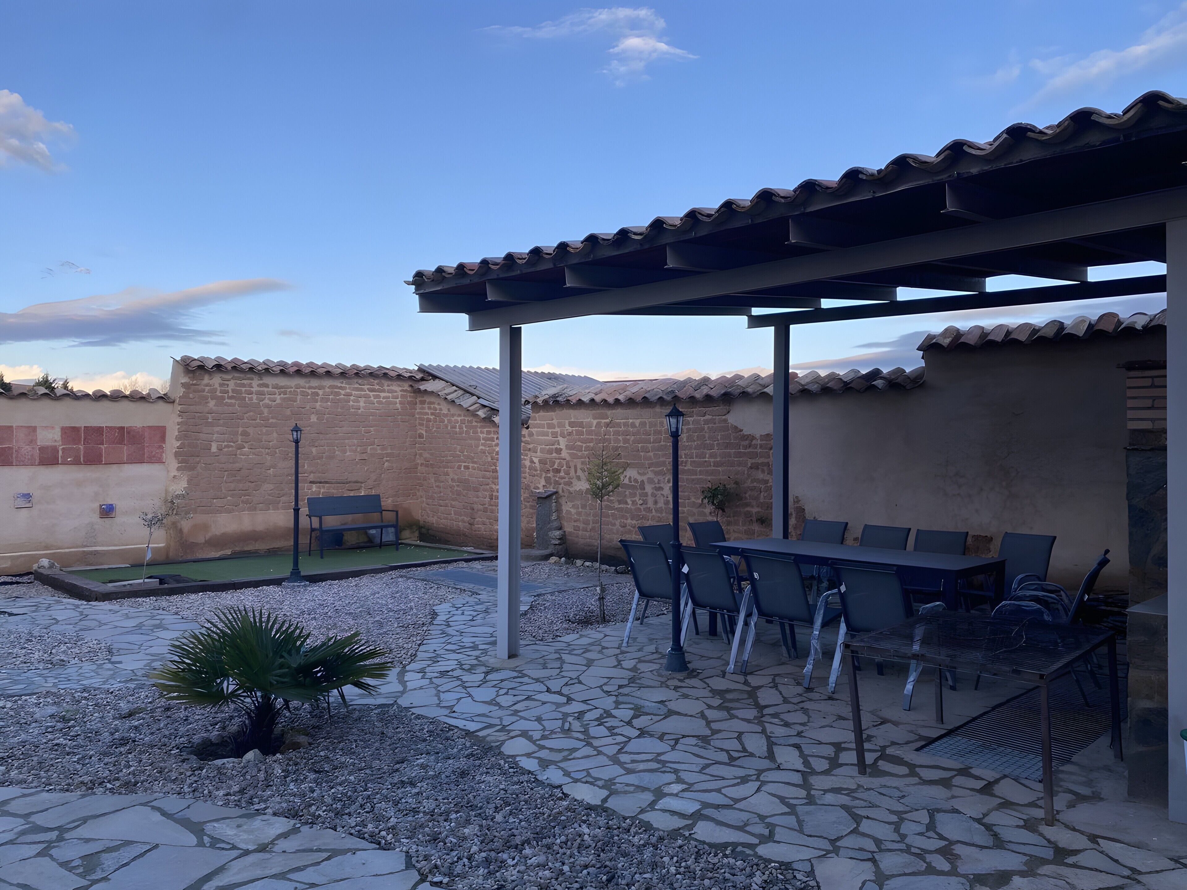 Un patio al aire libre con mesa y sillas, un pequeño jardín y suelo de baldosas de piedra.